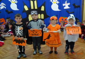 Dzieci w przebraniach halloweenowych stoją w rzędzie z halloweenowymi obrazkami.